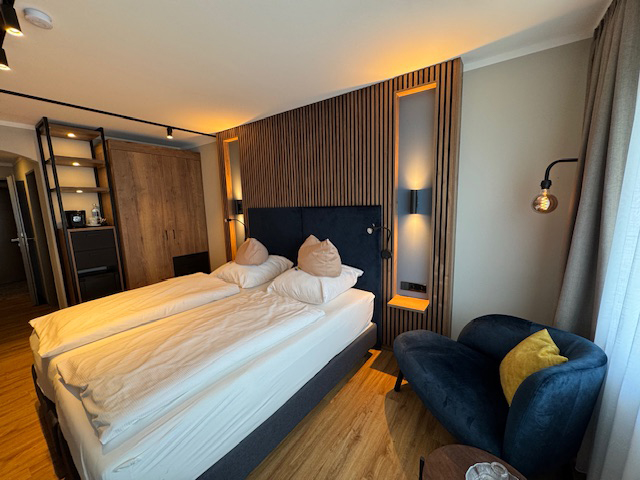 Doppelzimmer im Hotel Ennen, Blick auf das Boxspringbett und Sessel, im Hintergrund sind Holzpaneelen.