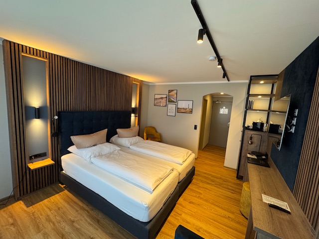 XL Doppelzimmer im Hotel Ennen, Gesamtaufnahme des Zimmers mit Bett, Schreibisch, Regal, Sessel und Flur.